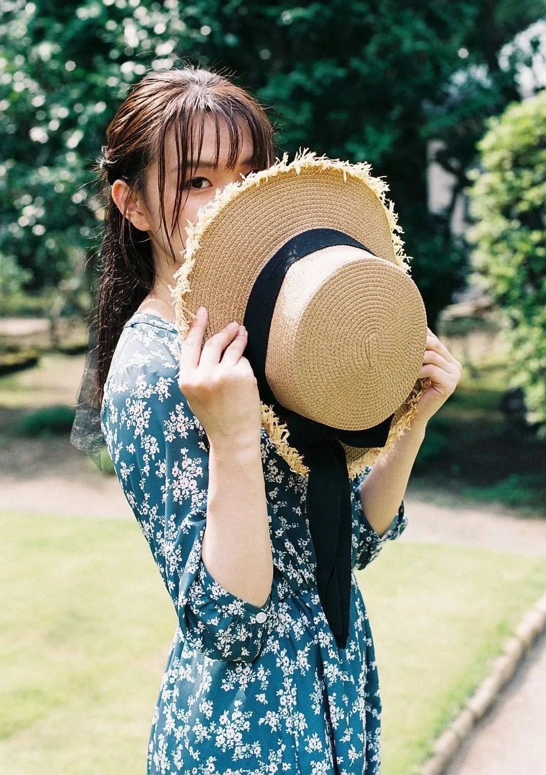 麦わら帽子で顔を半分隠して微笑む、たにもとまゆ